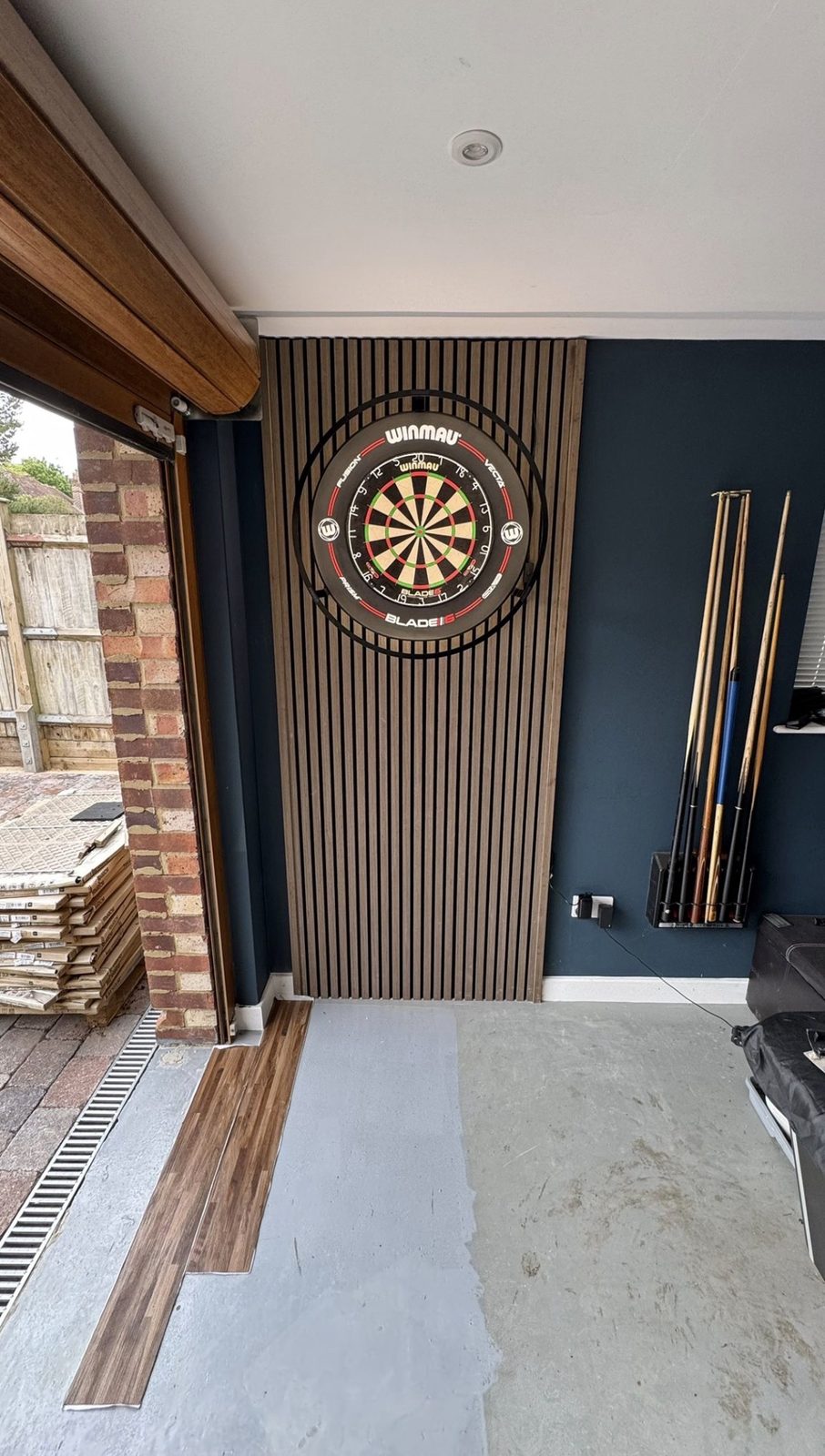 The same wall after installation, with slatted acoustic panel and mounted dartboard